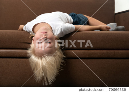 Child lies on the couch with his head hanging down. Boy is tired of lessons Child lies on the couch with his head hanging down. Boy is tired of lessons 70866886
