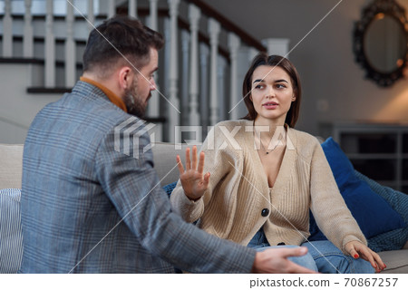 Upset couple at home. Handsome man and beautiful young woman are having quarrel. Sitting on sofa together. Family problems. Upset couple at home. Handsome man and beautiful young woman are having quarrel. Sitting on sofa together. Family problems. 70867257