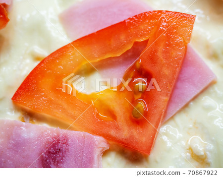 Closeup photo of a triangular slice of red tomato and slices of ham lying on the dough 70867922