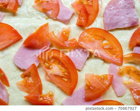 Close-up photo of slices of ripe tomatoes and juicy ham lying on a raw baking dough 70867927