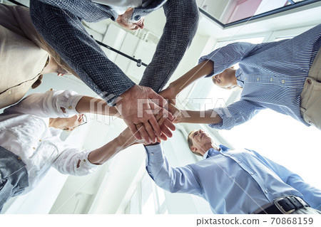 Bottom view of business people putting hands together, celebrating success while standing in the office Bottom view of business people putting hands together, celebrating success while standing in the office 70868159