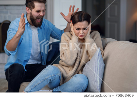 Defenseless upset woman closes her ears while her husband yelling at her sitting behind. Family relationship problems concept. 70868409