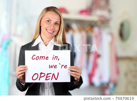 Happy woman holding a white banner with welcome sign. Come in, we are open Happy woman holding a white banner with welcome sign. Come in, we are open 70870619