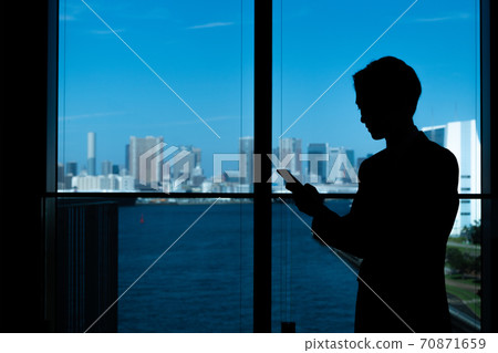 Image of a male businessman in silhouette with a smartphone Image of a male businessman in silhouette with a smartphone 70871659