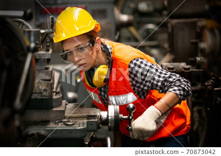 Female technician worker in uniform working on cnc machine in manufacturing.	 70873042
