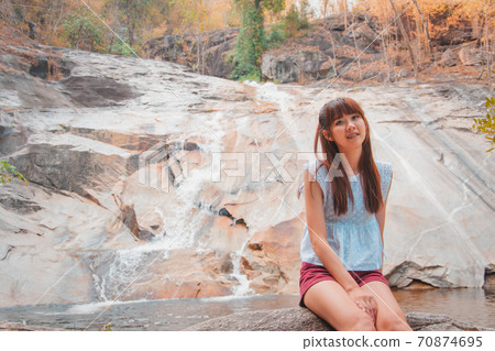 Asian woman travelers are smiling and relaxes sitting on the stone in front of the waterfall at Namtok Kaew Chan., Ratchaburi, Thailand. 70874695