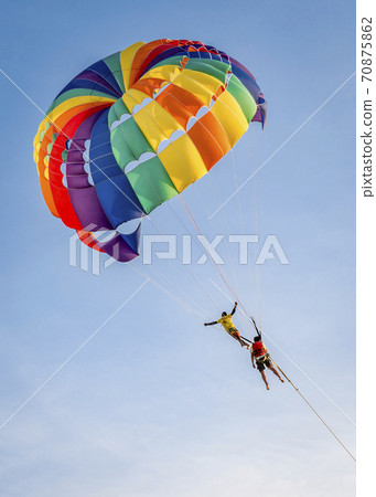 Flying a parachutist with an instructor on a colored parachute on a blue sky background Flying a parachutist with an instructor on a colored parachute on a blue sky background 70875862