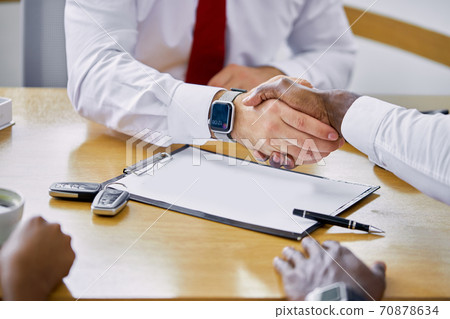 caucasian dealer giving key to new owner and shaking hands in auto show or salon 70878634