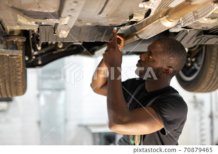 young male car mechanic in uniform checking car in automobile service with lifted vehicle young male car mechanic in uniform checking car in automobile service with lifted vehicle 70879465