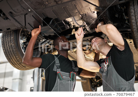 two interracial diverse mechanics checking car bottom two interracial diverse mechanics checking car bottom 70879467