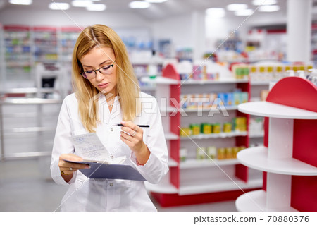 young good-looking woman pharmacist searching for medication on pharmacy shelves 70880376