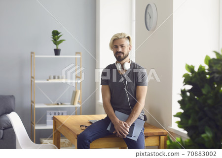 Handsome guy with notebooks and headphones sitting on table at home office. Online education, work, communication Handsome guy with notebooks and headphones sitting on table at home office. Online education, work, communication 70883002