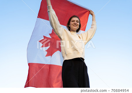 A beautiful young woman with the flag of Canada goes against the background of the forest. Canadian patriot smiles and looks into the camera 70884954