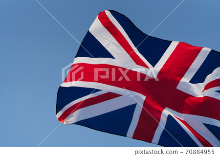 The flag of Great Britain develops in the wind at sunset against the sky. National symbol of England The flag of Great Britain develops in the wind at sunset against the sky. National symbol of England 70884955