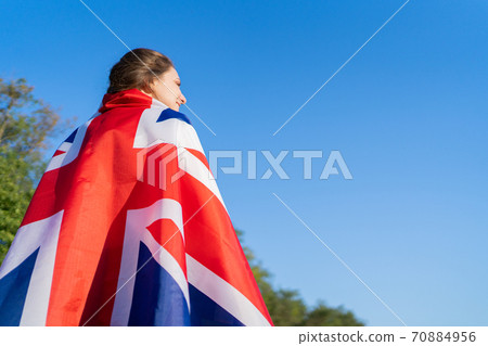 A British woman stands with the national flag on her back and looks into the distance. British independence, female patriot in a free country 70884956