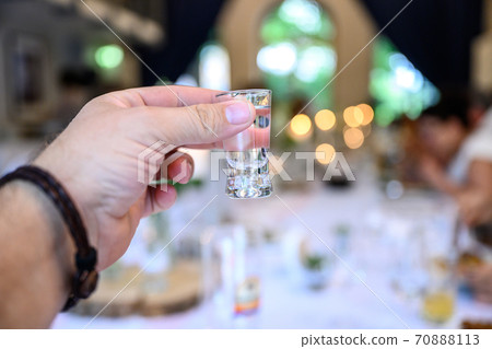 Wedding or party concept. Hand with a glass of vodka guest makes a toast, raising a glass 70888113