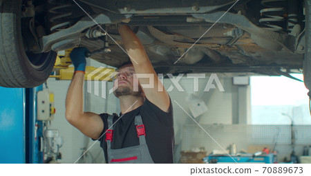 Auto mechanic working underneath car lifting machine at the garage. Auto repair shop, Car service, repair. Auto mechanic working underneath car lifting machine at the garage. Auto repair shop, Car service, repair. 70889673