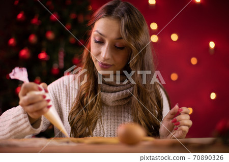 Traditionalist concept. pretty brunette young woman icing Christmas gingerbread 70890326