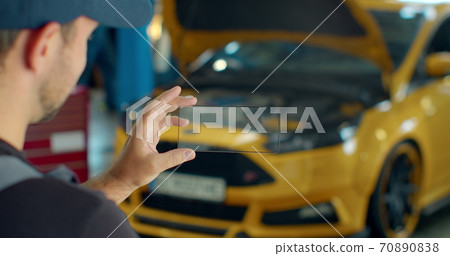 Car Service Manager Uses a smartphone transparent hologram digital display application in a car service. Professional car mechanic is working with diagnostics gadget on a vehicle in a service. Car Service Manager Uses a smartphone transparent hologram digital display application in a car service. Professional car mechanic is working with diagnostics gadget on a vehicle in a service. 70890838