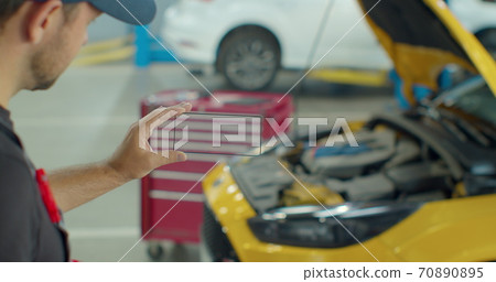 Car Service Manager Uses a smartphone transparent hologram digital display application in a car service. Professional car mechanic is working with diagnostics gadget on a vehicle in a service. Car Service Manager Uses a smartphone transparent hologram digital display application in a car service. Professional car mechanic is working with diagnostics gadget on a vehicle in a service. 70890895