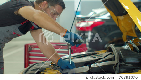 Car mechanic repairing a car with socket wrench. Car mechanic using a screw wrench to tighten the screws of an engine part. 70891070