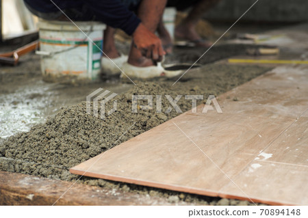 Selective focus on the texture of mixed cement and dirty surface of floor tiles in the house under construction with blurred worker in background 70894148
