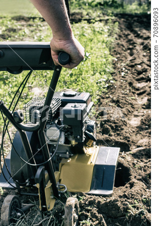 A motor cultivator plowing a raw in gerden soil vertical A motor cultivator plowing a raw in gerden soil vertical 70896093