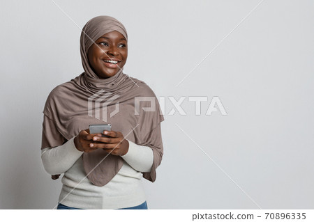 Mobile Offer. Cheerful Black Muslim Woman Holding Smartphone, Standing Over Light Background 70896335
