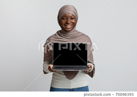 Cheerful African Muslim Woman In Hijab Holding Laptop With Blank Black Screen Cheerful African Muslim Woman In Hijab Holding Laptop With Blank Black Screen 70896393
