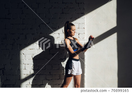 Beautiful contrasting portrait with the play of light and shadow of a young and fit girl in a loft interior with a white brick wall Beautiful contrasting portrait with the play of light and shadow of a young and fit girl in a loft interior with a white brick wall 70899165
