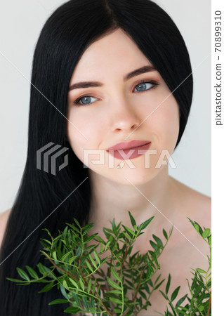 Portrait of beautiful woman's face with bouquets of green foliage over light gray background. 70899310