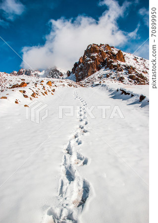 Deep marks in white snow. Snow tops and clouds amid blue skies. Winter mountain travel concept 70899950