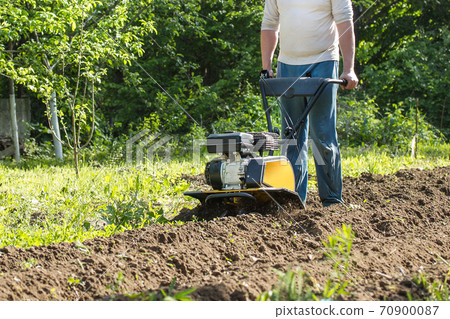 A man plowing garden soil by motor cultivator A man plowing garden soil by motor cultivator 70900087