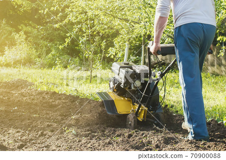A man plowing a garden soil by motor cultivator perspective view A man plowing a garden soil by motor cultivator perspective view 70900088