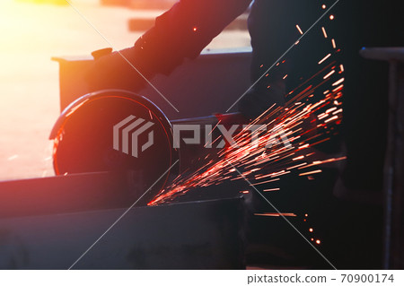 Professional worker cuts metal by angle grinder machine. Fountain of sparks. Fire safety at construction site. Professional worker cuts metal by angle grinder machine. Fountain of sparks. Fire safety at construction site. 70900174