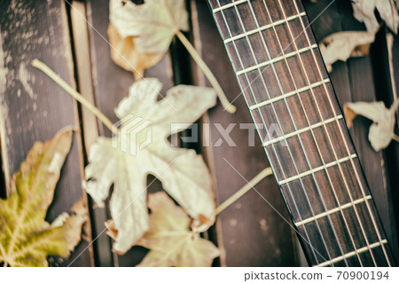 Close-up view of a fragment of acoustic classical guitar with fall maple leaf on wooden background. Autumn concept. 70900194