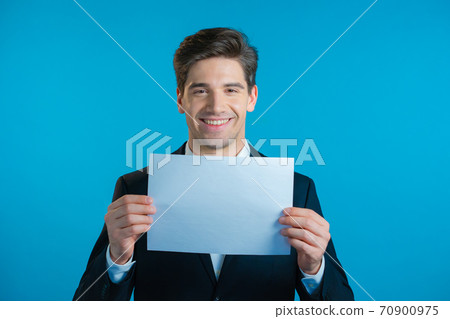 Portrait of young handsome businessman in suit holding white a4 paper isolated on blue studio 70900975