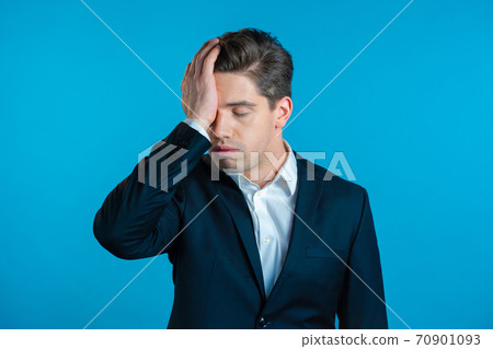 Frustrated european business man in suit over blue wall background. Guy is tired, bored of work or 70901093