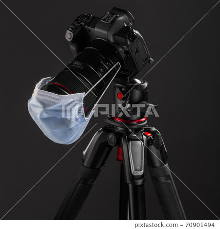 Professional photography equipment, digital mirrorless camera on tripod with surgical or protectiion mask. Illustrative photo of what covid-19 measures do with photography profession Professional photography equipment, digital mirrorless camera on tripod with surgical or protectiion mask. Illustrative photo of what covid-19 measures do with photography profession 70901494