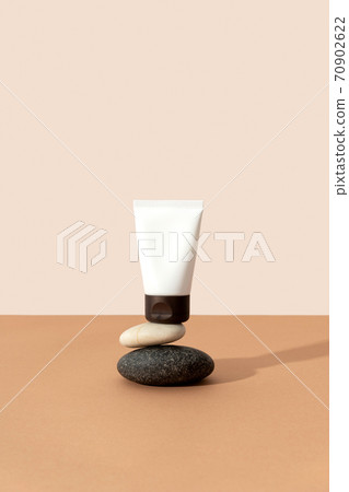 Bottles of cosmetic cream with balancing stones on beige background in sunlight Bottles of cosmetic cream with balancing stones on beige background in sunlight 70902622