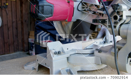 carpenter in protective gloves cuts off wooden oak bar on mitre saw close-up carpenter in protective gloves cuts off wooden oak bar on mitre saw close-up 70902914
