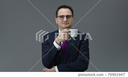 Handsome confident middle aged man holding cup of coffee and looks at camera Handsome confident middle aged man holding cup of coffee and looks at camera 70902947