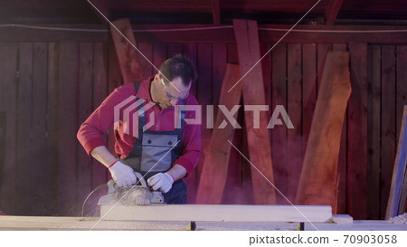 Carpenter cleans surface of wooden beam with electric planer and flies sawdust Carpenter cleans surface of wooden beam with electric planer and flies sawdust 70903058