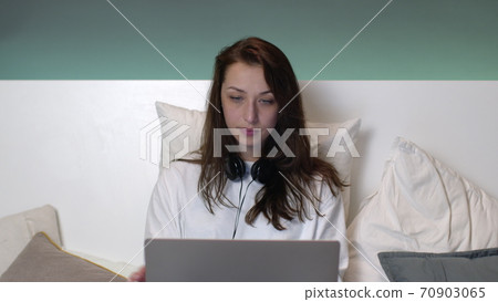 Attractive caucasian woman with long hair in pajamas in bed works on a laptop. 70903065