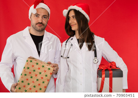 two doctors in Santa Claus hats hold Christmas gift boxes looking at camera 70903451