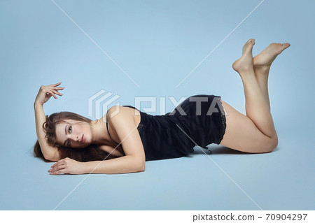 attractive brunette with crossed legs lying down posing in the Studio on a blue background attractive brunette with crossed legs lying down posing in the Studio on a blue background 70904297