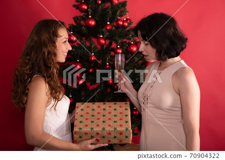 attractive young lesbian couple give gifts at Christmas tree drinking champagne attractive young lesbian couple give gifts at Christmas tree drinking champagne 70904322