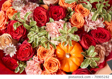 Red and orange flowers with pumpkin. Autumn bouquet of mixed flowers in glass vase on wooden table. The work of the florist at a flower shop. Fresh cut flower. Red and orange flowers with pumpkin. Autumn bouquet of mixed flowers in glass vase on wooden table. The work of the florist at a flower shop. Fresh cut flower. 70905282