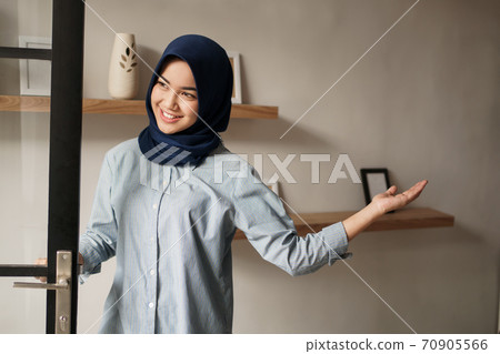 you are welcome. cheerful mature woman in welcome sign and smiling while standing against front door 70905566