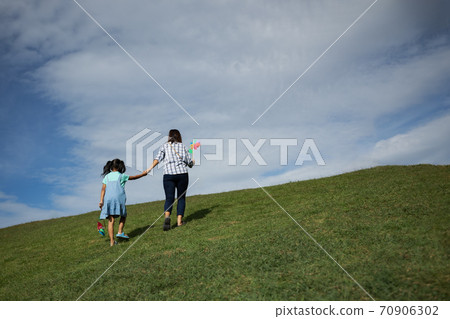 Mother and daughter holding turbine toy and holding hand together going up to the top of the hill to enjoy with beautiful nature. Mother and daughter holding turbine toy and holding hand together going up to the top of the hill to enjoy with beautiful nature. 70906302